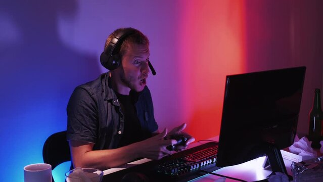 Cyber winning. Online competition. Entertainment drive. Happy expressive male playing computer using joypad feeling euphoric in dark light home interior.
