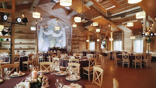 Wide shot wooden banquet hall with decorations and banquet tables. Beautiful wedding decoration with vintage lamps. A large hall for celebrations, the camera flies back