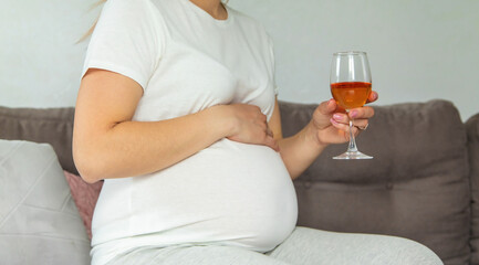 A pregnant woman drinks wine in a glass. Selective focus.