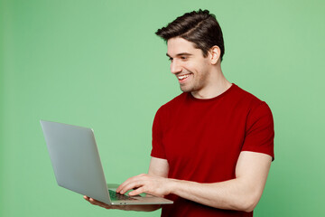 Young smiling happy smart IT man he wearing red t-shirt casual clothes hold use work on laptop pc...