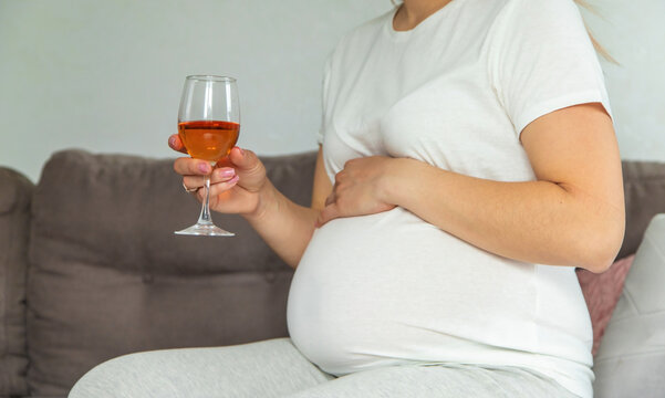 A pregnant woman drinks wine in a glass. Selective focus.