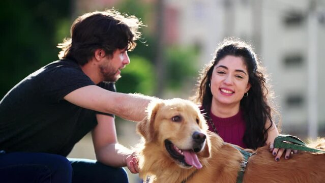 Happy couple enjoying sunny day with their Golden Retriever Dog Pet outdoors. Man and woman petting their canine companion