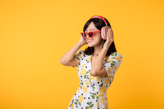 Smile pretty asian model person listen music song and enjoy dance with wireless headphone online audio radio sound. Positive fun exited joyful youth female woman on yellow isolated background studio
