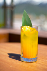 A glass with a cocktail, juice, lemonade on a table in the mountains. Rest. Relax. Fruity drink decorated with green leaf and orange chips.