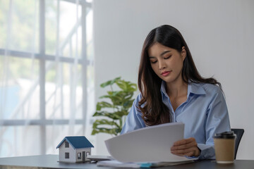 Accountant, real estate agent, Asian business woman handing model house and key to customers along with house interest calculation documents for customers to sign.