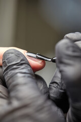 the master makes a manicure with a gel polish coating for a woman with clean nails. a master in black latex gloves paints a nail with black varnish