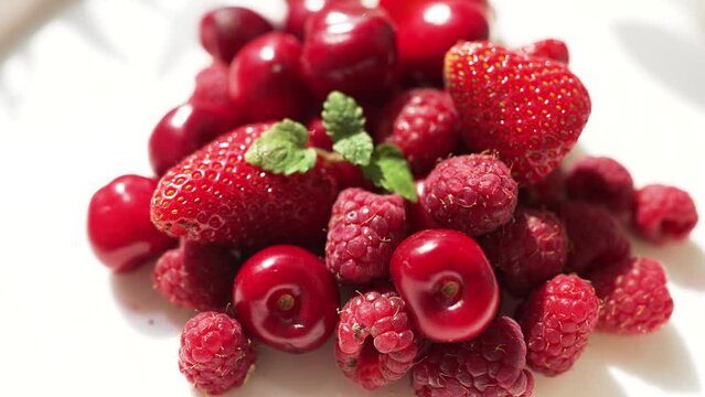 Juicy fresh raspberries strawberries and cherries lie on a white plate