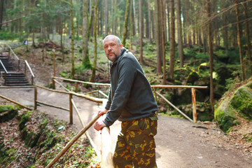 Old hiker standing on the forest background and looking away, traveler man taking break after long way, adventure and extreme sport