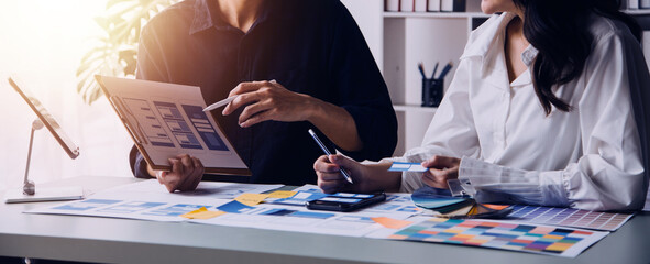 Close up ux developer and ui designer brainstorming about mobile app interface wireframe design on table with customer breif and color code at modern office.Creative digital development agency