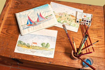 Watercolor painting, a light and immediate way to record your travel impressions. Some artwork and tools on a rustic wooden chest of drawers.