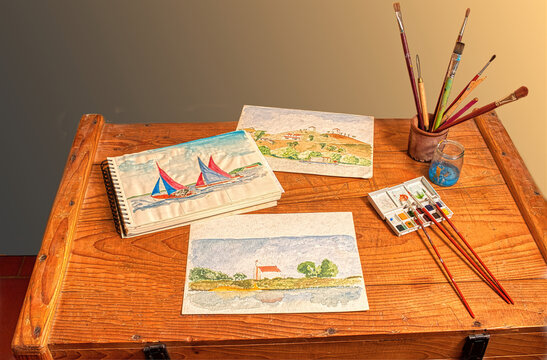 Watercolor painting, a light and immediate way to record your travel impressions. Some artwork and tools on a rustic wooden chest of drawers.
