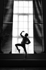 Obraz na płótnie Canvas Full length image of a dancer in position , posing near window. Black and white image