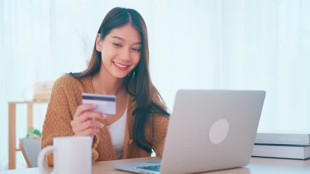 Young woman pressed the credit card code to pay online via the laptop on the desk at home, Online purchases and use of credit cards concept.