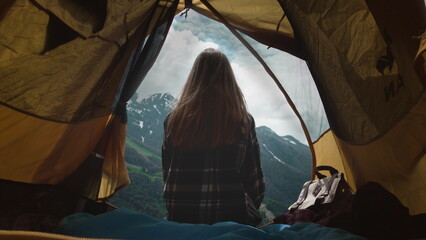 A girl hiker dressed in a plaid shirt sits resting in a yellow tent. Slow motion hair, outdoor adventure lifestyle.
