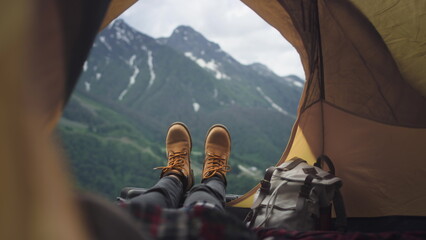 Women's legs in yellow hiking boots lie in a yellow tent. The traveler is resting, admiring the...