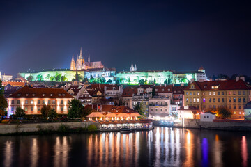 View of Prague Castle and surrounding buildings at night. Reflections of colorful city lights in the river. Prague, Czech Republic.