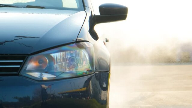 The Car Is Watered With Water From A Washing Gun At A Car Wash. Splashes Of Water Bounce And Scatter In Different Directions. Headlight Close-up