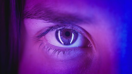 Extreme close-up Beautiful girl opens one eye, neon pink blue light. Attractive feminine look....