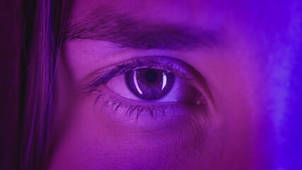 Extreme close-up Beautiful girl opens one eye, neon pink blue light. Attractive feminine look....