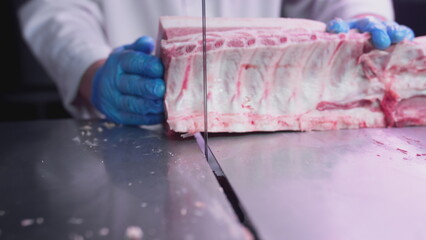 Industrial processing of meat. A man cook cuts a piece of tenderloin in a butcher's shop on a machine with a band saw. Ribeye or marbled beef. - obrazy, fototapety, plakaty