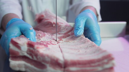 Industrial processing of meat. A man cook cuts a piece of tenderloin in a butcher's shop on a machine with a band saw. Ribeye or marbled beef.