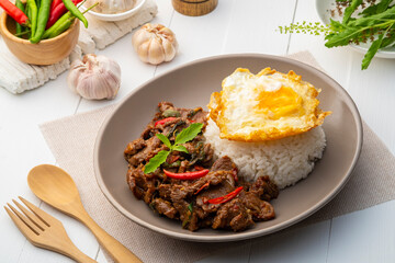 Stir fried sliced Beef with Holy Basil and Cooked Rice topped with fried egg in white plate.Thai spicy food(Pad Kra pao)