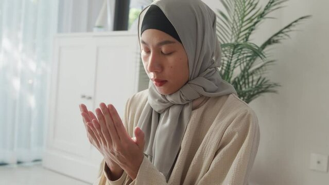 Close-up Asia muslim woman hand pray doa communicate to allah wear prayer clothes green mukena cover hijab in living room at home, pray room bright light, Islamic faith, Ramadan Kareem, Eid Mubarak.