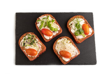Red beet bread sandwiches with tomatoes and microgreen on black board isolated on white. top view.