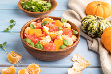 Fototapeta na wymiar Vegetarian fruit salad of pumpkin, tangerine, pomegranate, microgreen sprouts on blue, side view, close up.