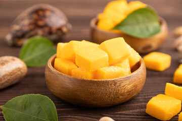 Dried mango cubes in wooden bowls on brown wooden, side view, selective focus.