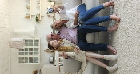 Happy senior grandpa, grandma and teen grandkid girl taking selfie on smartphone at home, shooting self video for social media, talking on video online conference call - Powered by Adobe