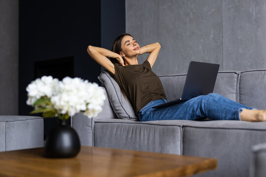 Young Relaxed Woman Resting While Sitting With Laptop On Sofa At Living Room