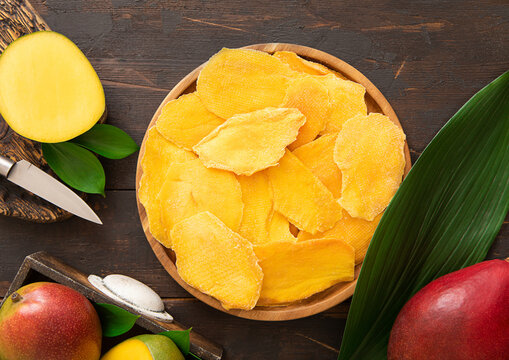 Round plate with dried mango pieces with knife and raw fruits.