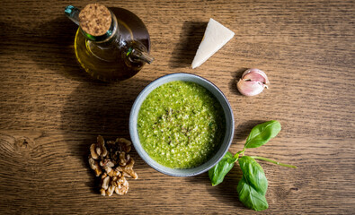 Freshly made green basil walnut pesto in a bowl surrounded by its ingredients.