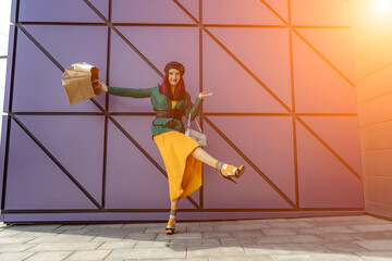 A happy shopaholic girl throws her bags near a shopping center.