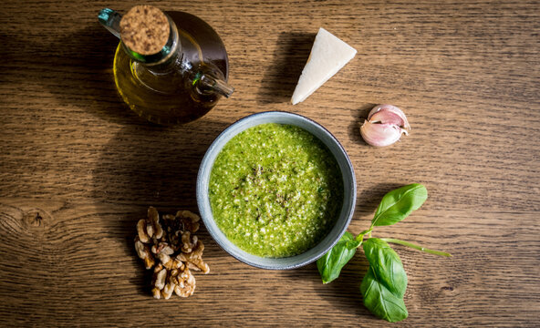 Freshly made green basil walnut pesto in a bowl surrounded by its ingredients.