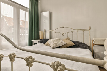 a bed in a bedroom with green curtains on the windowsills and an iron headboard that has been...