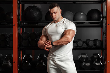 Muscular man looking at his watch in gym, schedule. Athletic male wears sportswear