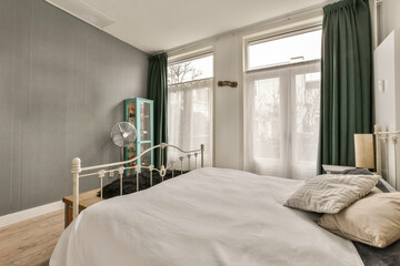 a bedroom with a bed and green drapes on the window is in the room has hardwood flooring, white walls
