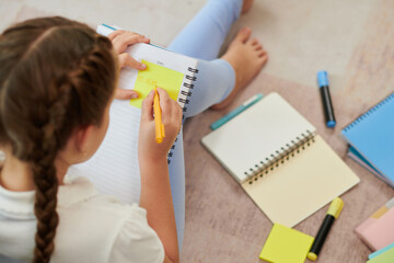 Schoolgirl writing important information on yellow stickers when preparing for school exams at home