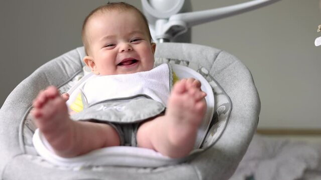 adorable baby eating first food, mother feeding from jar with spoon.infant toddler sitting in newborn electric automatic swing cradle.smiling with gum,no teeth,happy child. food diversification