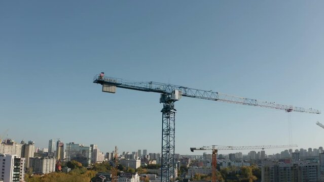 Top view of construction crane on background of city on sunny day. Stock footage. Construction cranes at height with view of city to horizon. Construction crane on background of modern city on sunny