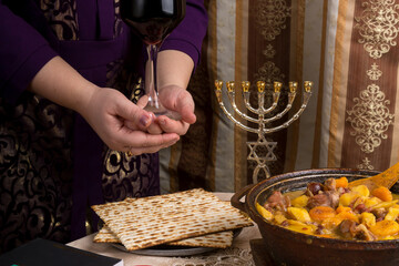 A woman at a table laid for a Passover seder holds a glass of red wine in her hands.