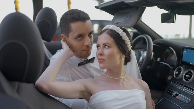 Couple of bride and groom in convertible. Action. Beautiful couple of newlyweds in car in summer. Couple plays newlyweds for photo shoot in convertible