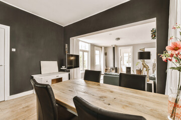 a dining room with black walls and wooden table, chairs and flowers in a vase on the end of the table