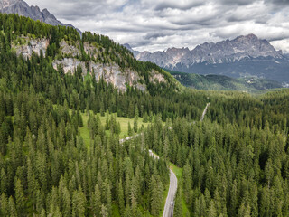 Aerial shot of a curvy road in a forest near the giau pass in the dolemite mountain range. Winding road in mountain valley under rainy clouds.