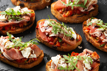 Parma ham and tomato bruschetta served on black slate with mozzarella, wild rocket leaves and...