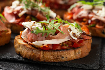 Parma ham and tomato bruschetta served on black slate with mozzarella, wild rocket leaves and...