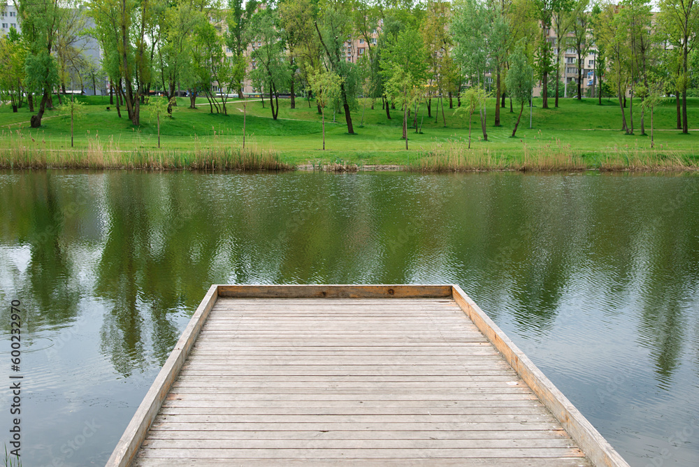 Poster Beautiful colorful summer natural landscape with a lake in park surrounded by green foliage of trees. Wooden pier in the foreground.