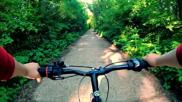 Man riding a bike on a road in the forest on summer sunny day. Person riding bicycle on pathway in nature. POV. Cycling outdoors natural park. Leisure entertainment sports recreation activity extreme